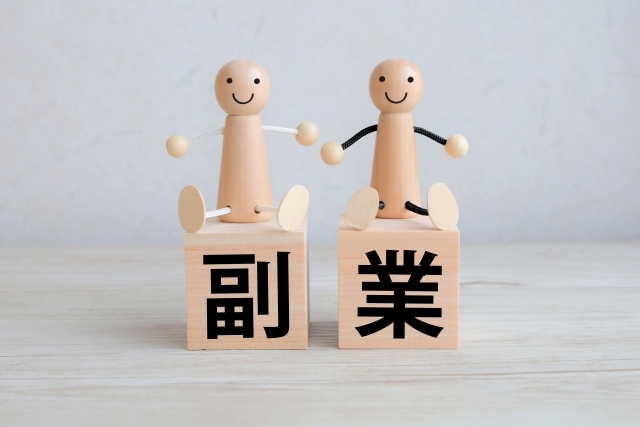 副業と印字された木製ブロックの上に座っているマスコット