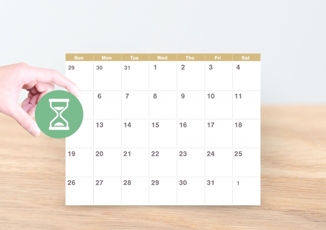 置き型カレンダーと砂時計のマークを持つ手元