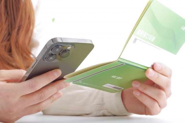 スマホと通帳を見比べている女性の手元