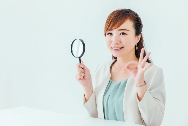 右手にルーペを持ってOKサインをしている女性