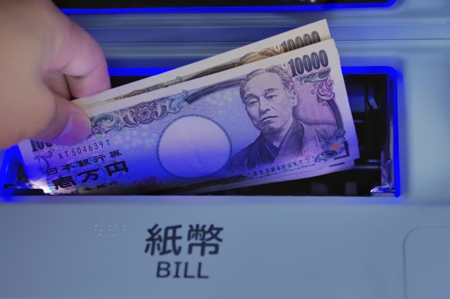 ATMの紙幣投入口と2万円を持っている人の手元