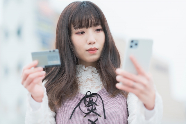 歩きながらクレジットカードとスマホを持つ女性